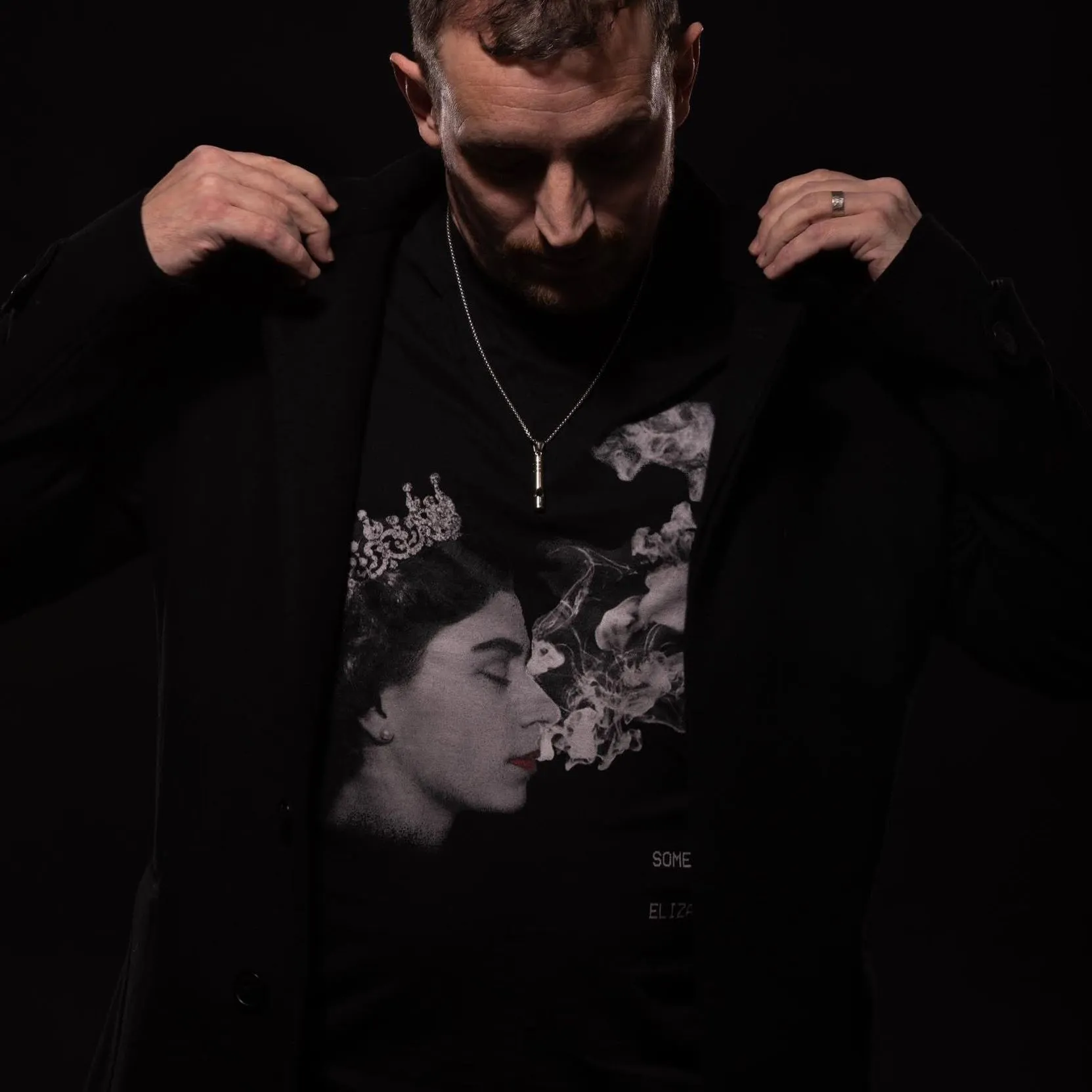 Carl Nicholson adjusting the lapels of a black jacket in a dark studio