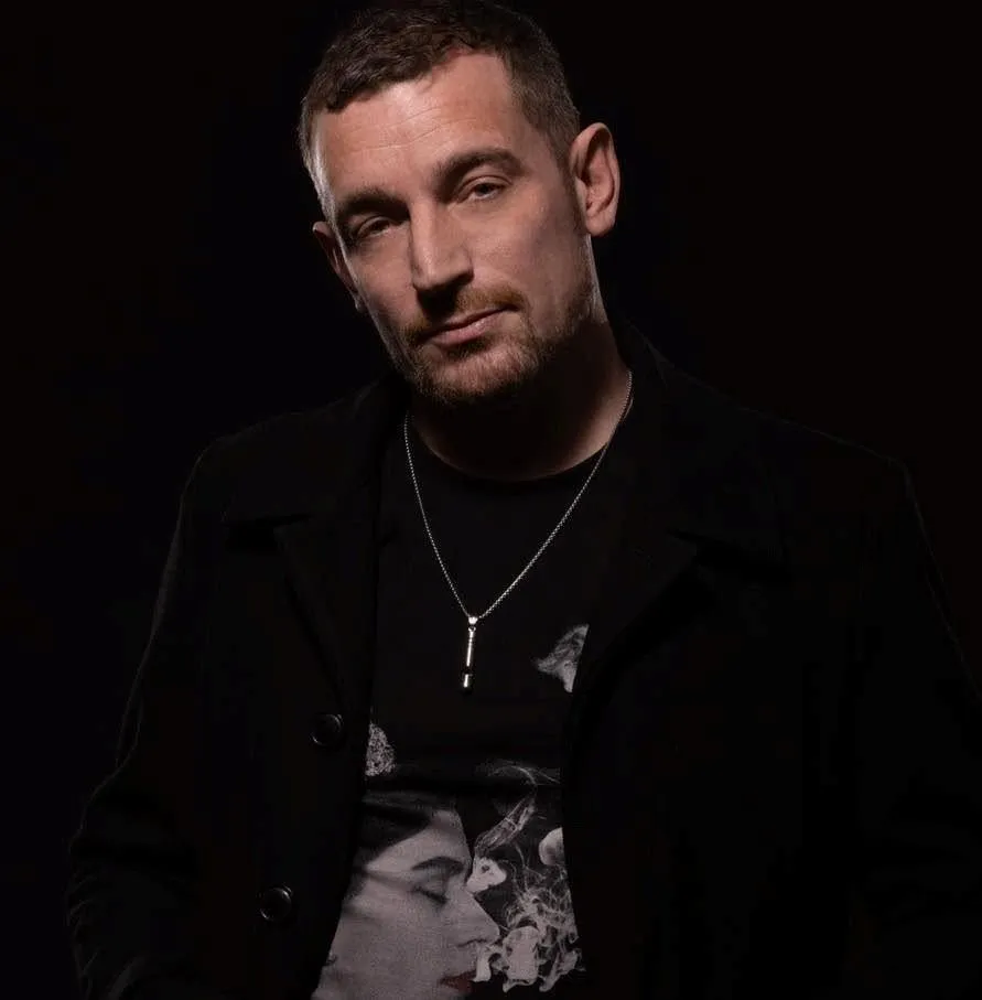 NICHOLSON in a black jacket, photographed against a dark background